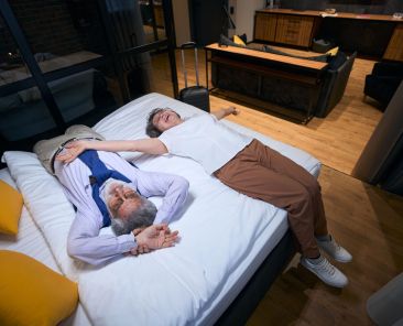 Tired from the road, but happy elderly spouses are resting on hotel bed, they stayed in a comfortable hotel room