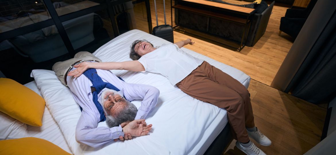 Tired from the road, but happy elderly spouses are resting on hotel bed, they stayed in a comfortable hotel room